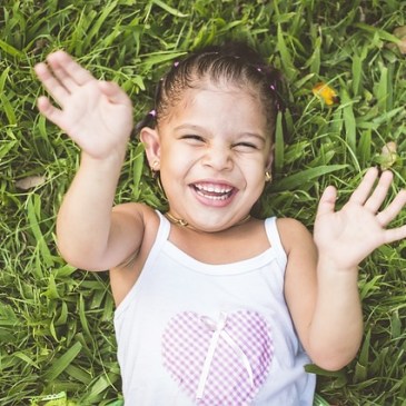 Little girl lying in grass looking up at camera and laughing