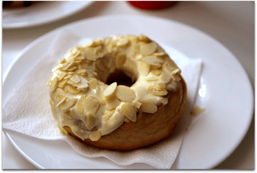 A doughnut with cream colored frosting and slivered almonds
